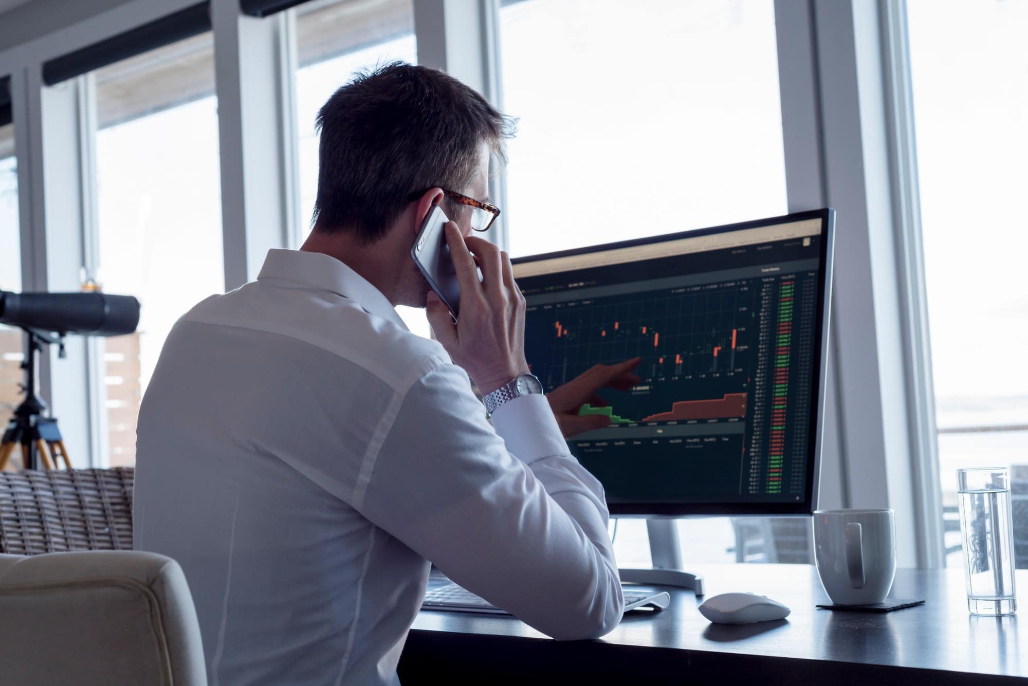 Businessman holding phone up to speak while discussing computer data